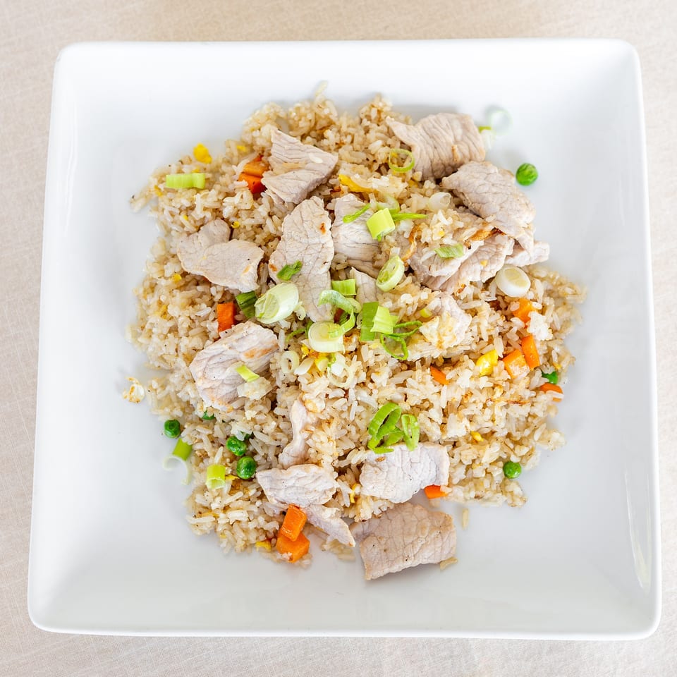 Pork fried rice with peas, carrots, scrambled egg, and sliced green onions on a white square plate.