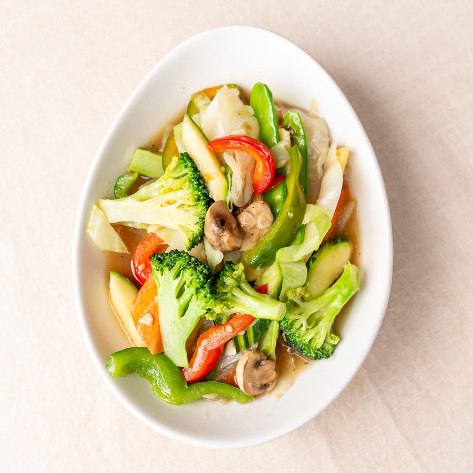Bowl of colorful stir-fried vegetables including broccoli, bell peppers, mushrooms, cabbage, zucchini, and carrots.