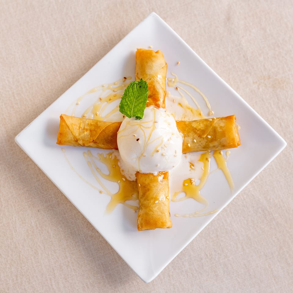 Golden fried pastries arranged around vanilla ice cream, drizzled with honey and sesame seeds, and garnished with fresh mint.