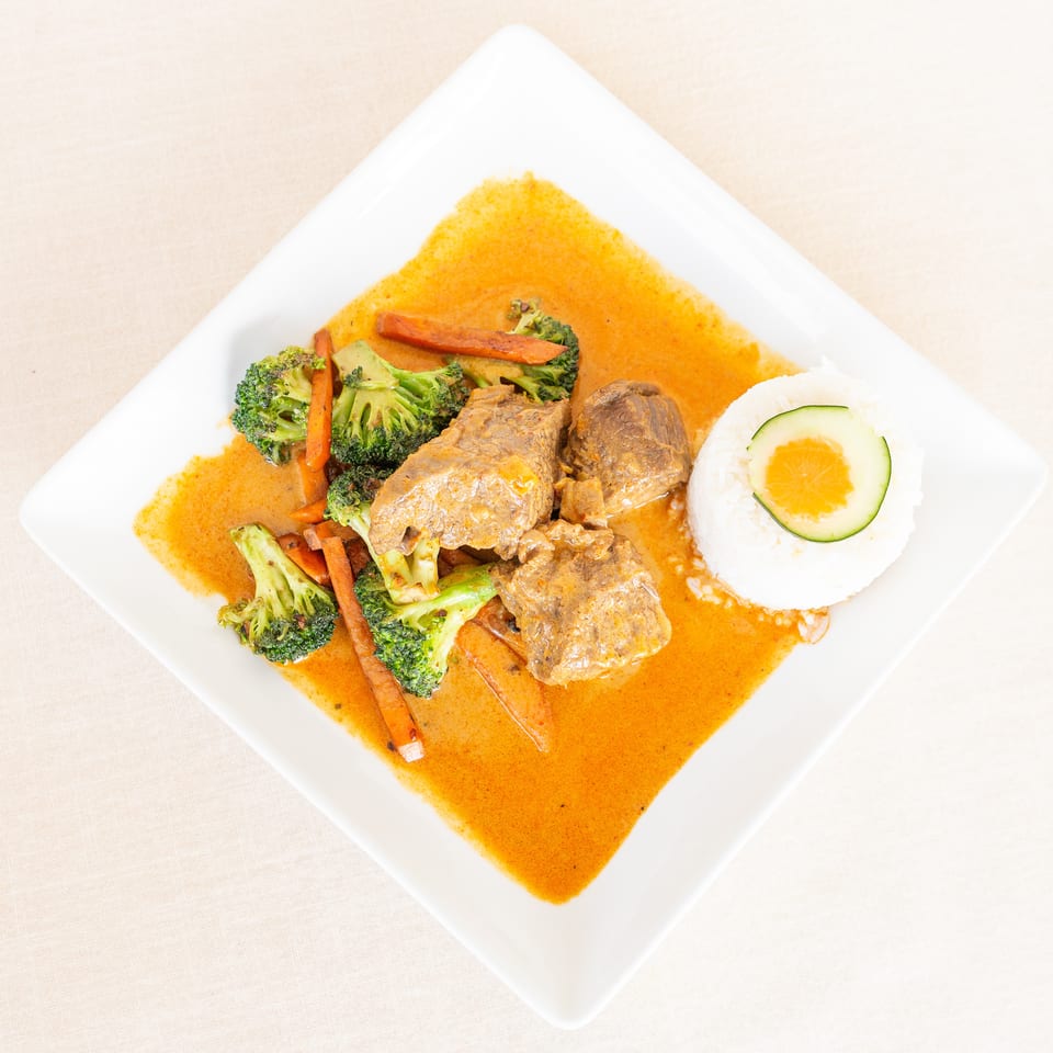 Sliced beef in orange sauce with broccoli, carrots, and white rice topped with a citrus slice on a square plate.